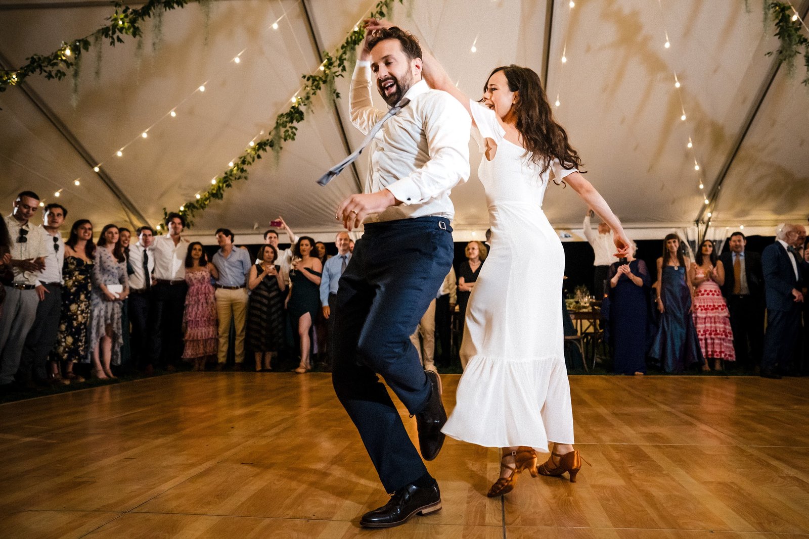 Couple dancing energetically on a wood dance floor at an outdoor tented New Orleans reception